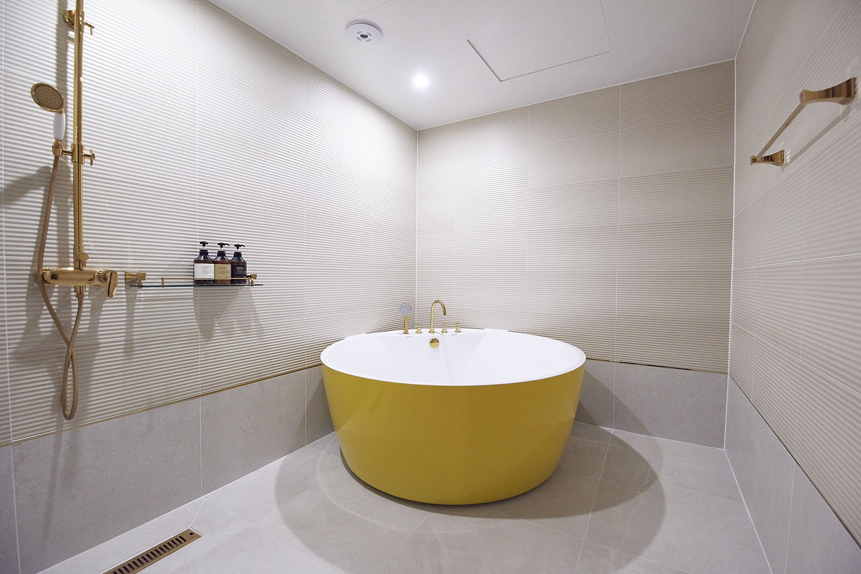 Un baño moderno con una bañera amarilla grande, un cabezal de ducha manual y un grifo de pared.