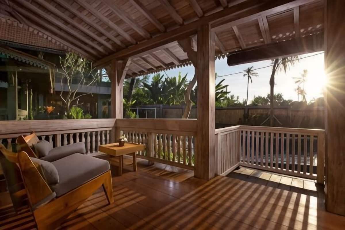 Um deck de madeira com sofá e mesa, vista para palmeiras, e um estilo arquitetônico tradicional.