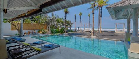 A poolside area with lounge chairs, a covered seating area, and a view of the beach and ocean.