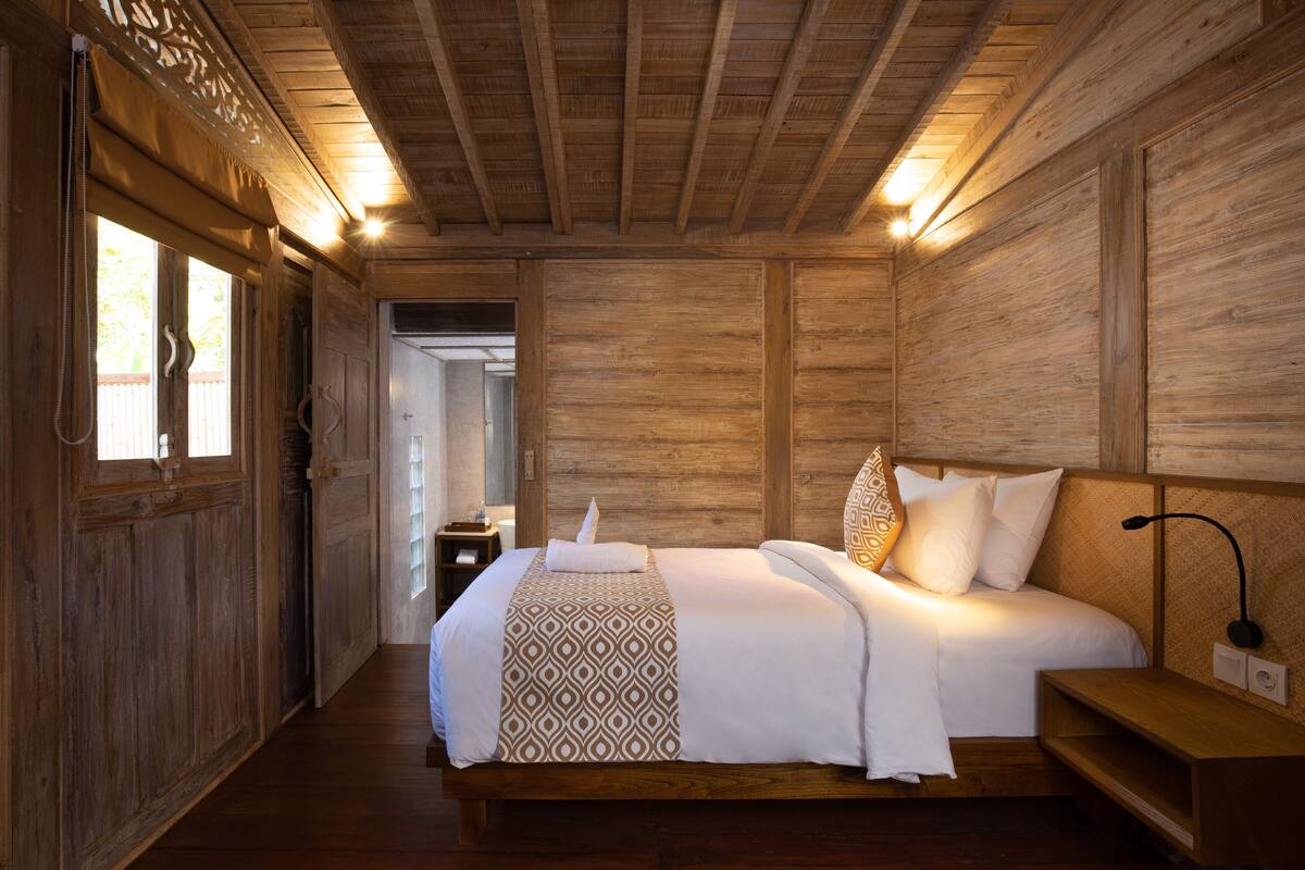 Quarto com painéis de madeira, uma cama grande, uma mesinha de cabeceira e um criado-mudo.