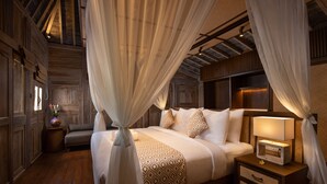 A bedroom with a canopy bed, bedside tables with lamps, and a wooden floor.