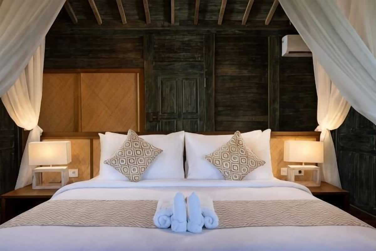Uma cama com dossel, duas mesas de cabeceira com luminárias, almofadas estampadas e arranjo de toalhas.
