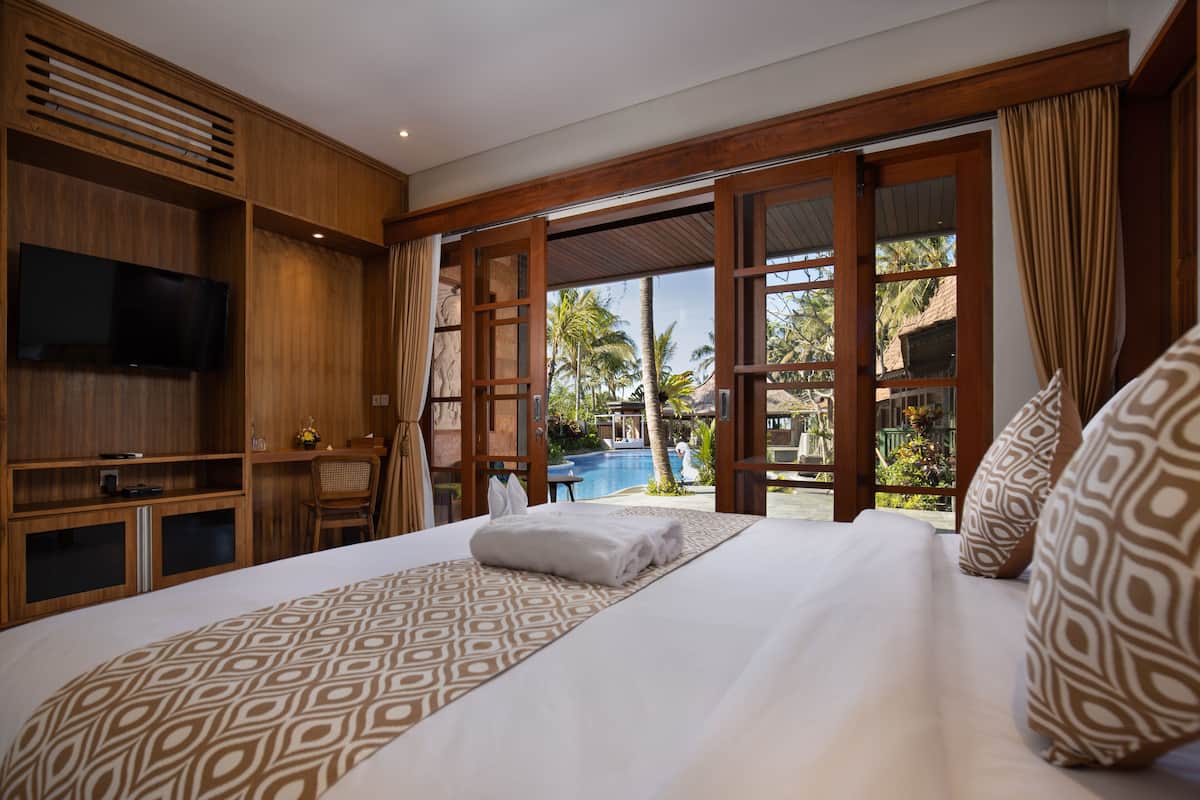 Quarto de hotel com uma cama grande, televisão, painéis de madeira e vista para uma piscina.