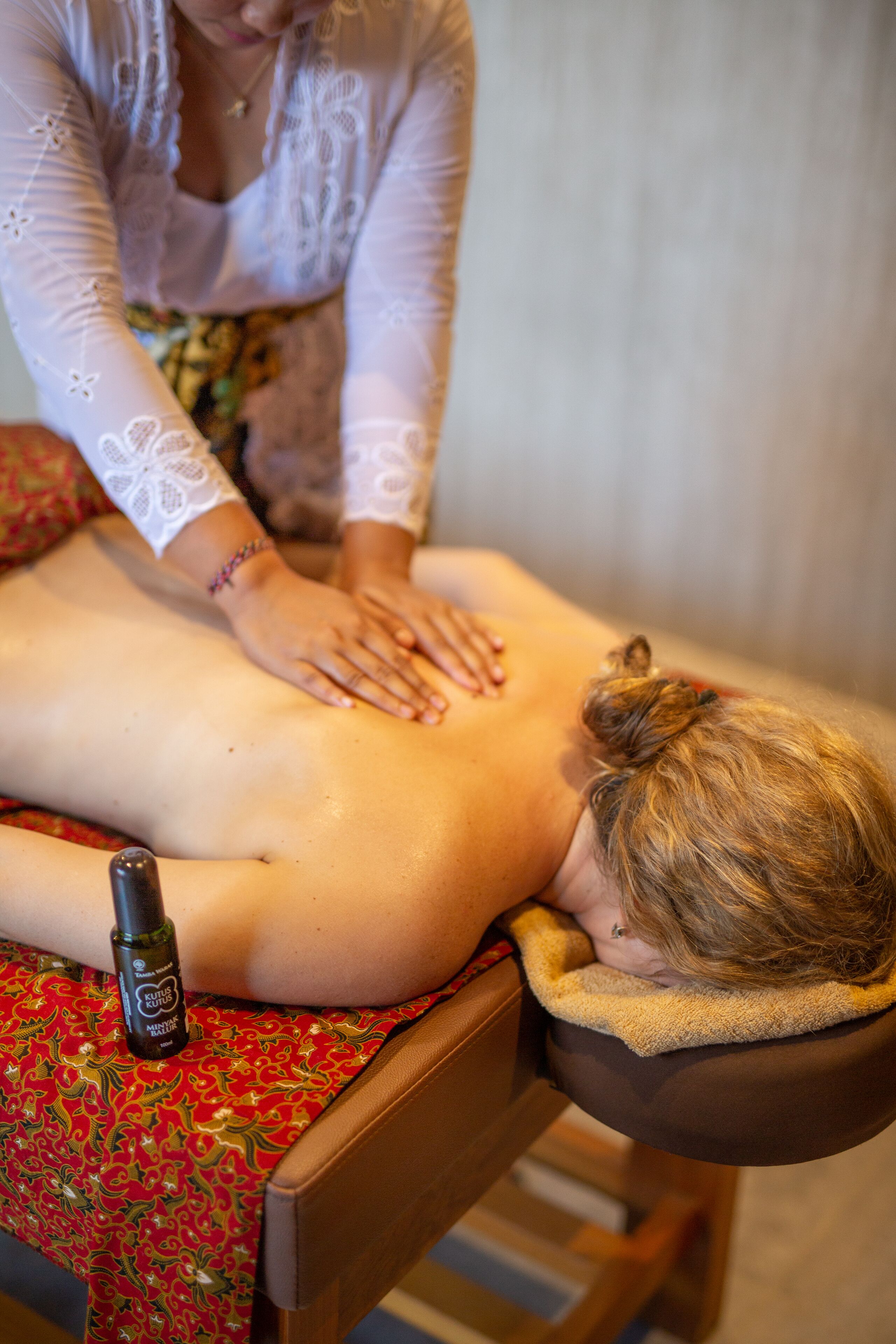 Una sesión de terapia de masajes en curso, con un cliente recostado en una camilla, un terapeuta aplicando presión y una botella de aceite de masaje sobre la mesa.