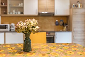 A kitchen with white cabinets, a microwave, and a vase with flowers on a table with a sunflower tablecloth.