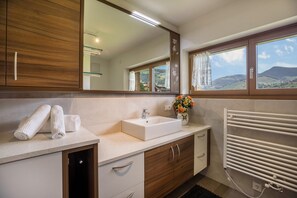 Un baño con tocador de madera, lavamanos blanco, espejo y vistas al exterior.