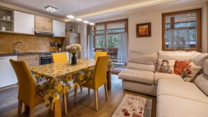 Una cucina moderna con elettrodomestici integrati, una zona pranzo con tavolo e sedie, e un soggiorno con divano e cuscini decorativi.