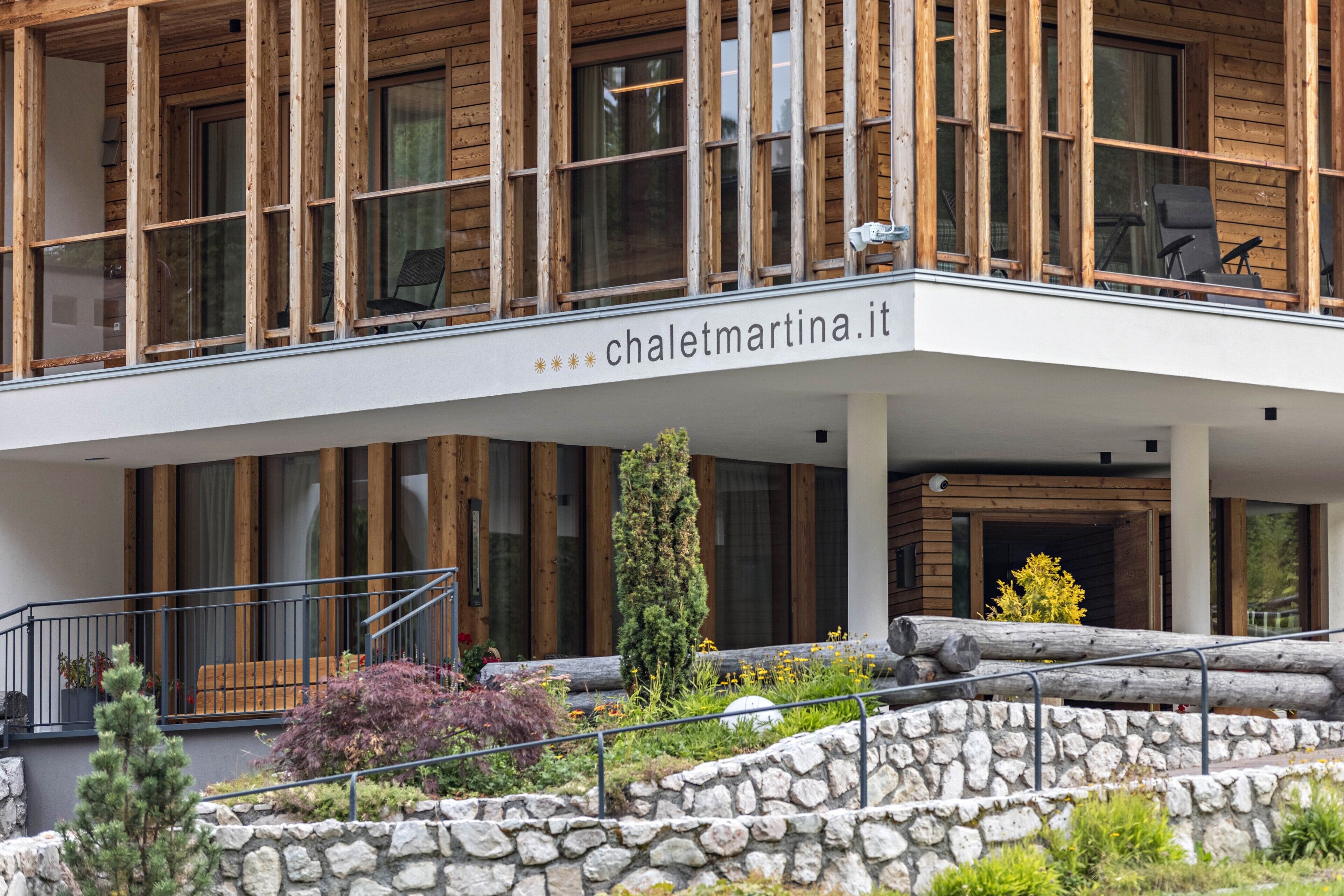 Un bâtiment moderne avec une façade en bois, un balcon agrémenté de chaises et une enseigne indiquant « chalematrina.it ».