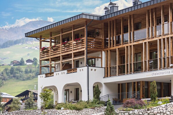 Un edificio moderno con balcón de madera, ventanas amplias y una pared de piedra.