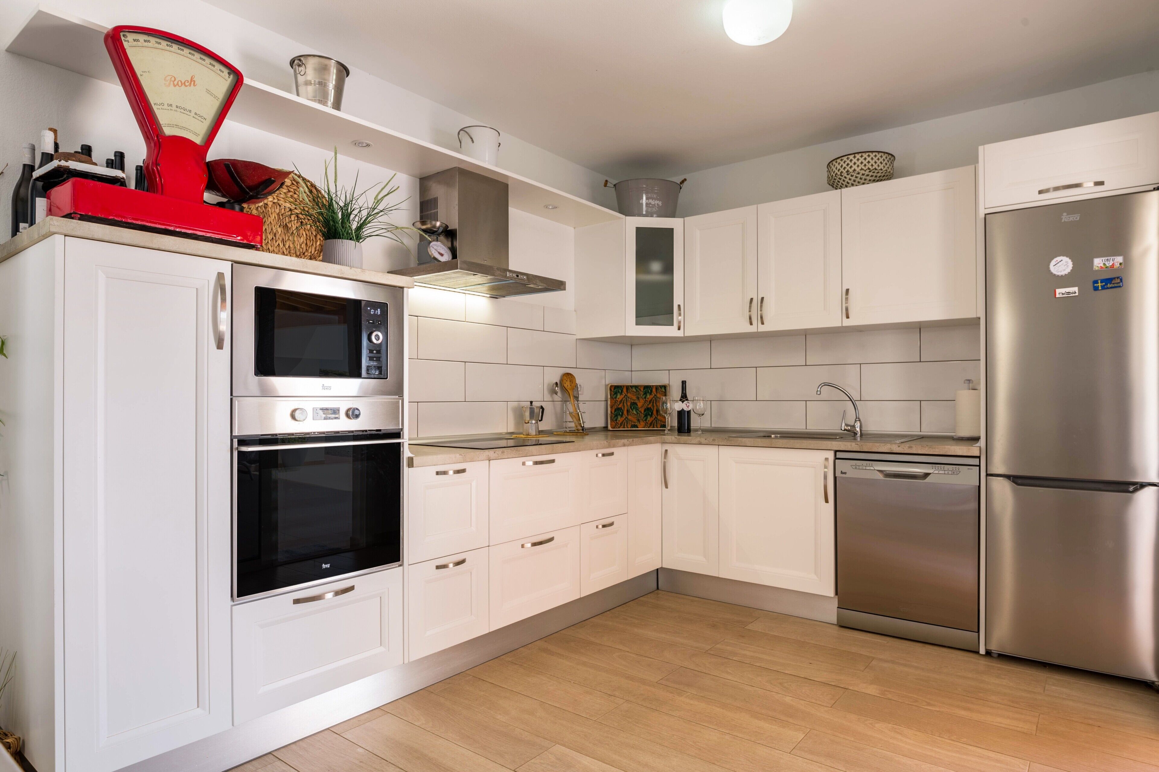 Una cocina moderna con armarios blancos, electrodomésticos de acero inoxidable y piso de madera.