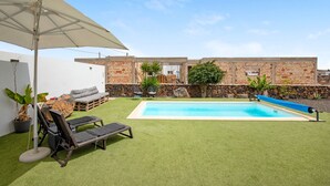 A backyard with a swimming pool, a lounge area, and a brick wall. - Holiday Home Casa Nati with Mountain View, Wi-Fi, Shared Garden (Lajares)