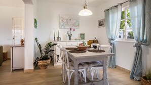 A dining area with a white table and chairs, a hanging light fixture, and a window with curtains. - Holiday Home Casa Nati with Mountain View, Wi-Fi, Shared Garden (Lajares)