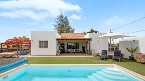 A swimming pool with a patio area, a covered seating area, and a white building with a tiled roof. - Holiday Home Casa Nati with Mountain View, Wi-Fi, Shared Garden (Lajares)