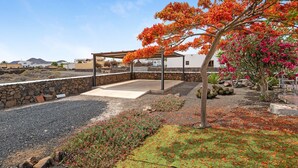 A covered outdoor area with a stone wall, a pergola, and a tree with orange leaves. - Holiday Home Casa Nati with Mountain View, Wi-Fi, Shared Garden (Lajares)