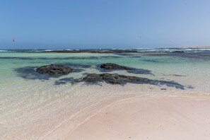 A beach with clear water, rocks, and a distant view of the ocean.
