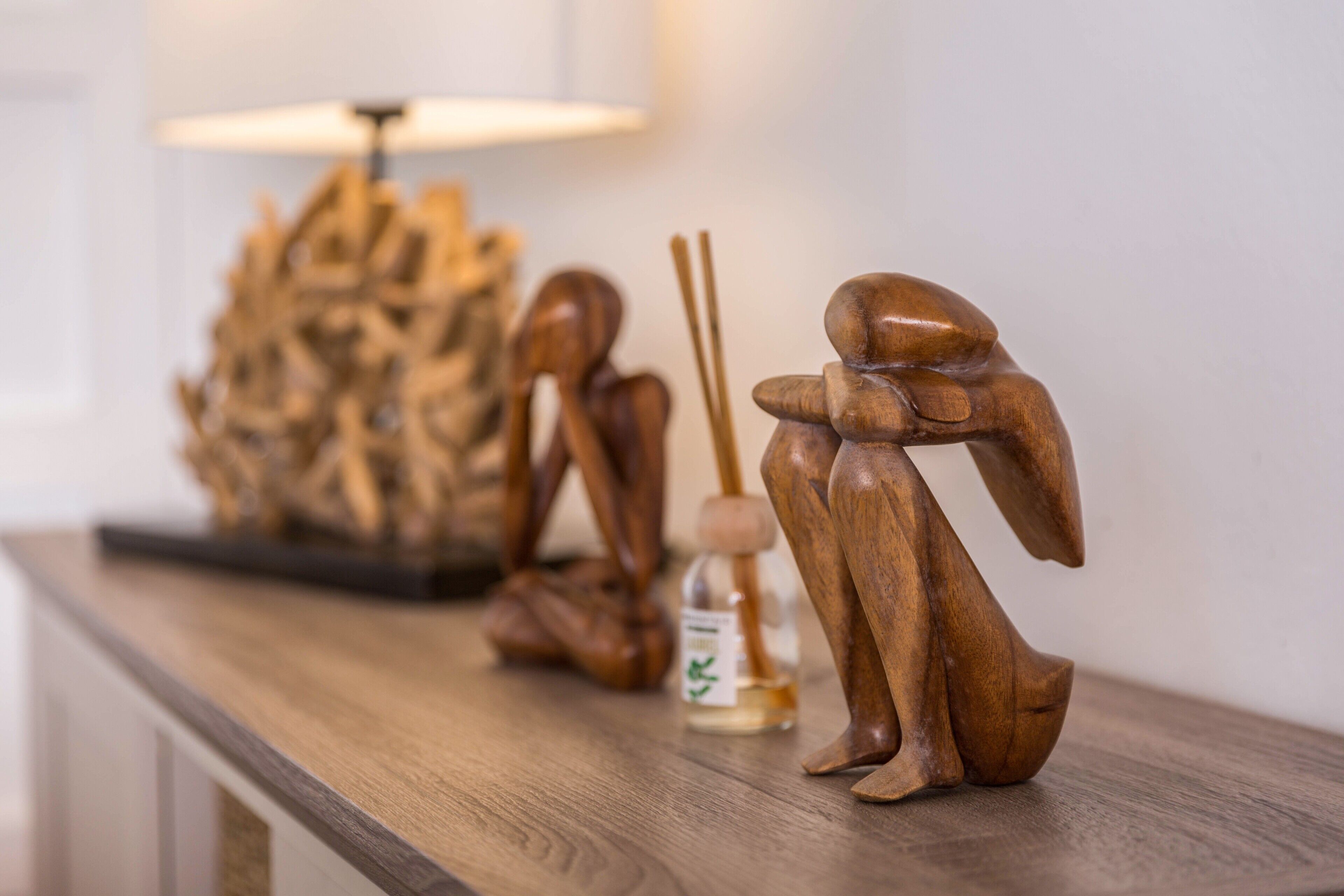 Een houten beeld van een figuur op een tafel, een lamp en een fles met etiket.