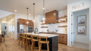 A modern kitchen with wooden cabinets, a central island with bar stools, pendant lighting, and a white backsplash.