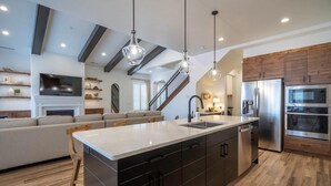 A modern kitchen with a central island, stainless steel appliances, and a wooden staircase.