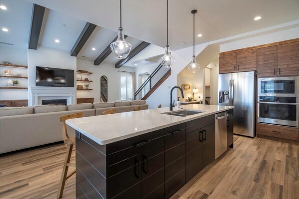 A modern kitchen with a central island, stainless steel appliances, and a wooden staircase.