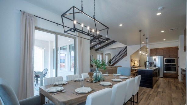 A modern dining area with a wooden table set for six, white chairs, and a hanging light fixture.