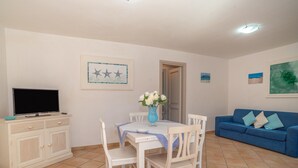 Un salon avec un téléviseur, une table à manger avec des chaises, un canapé bleu et des œuvres d’art accrochées aux murs.