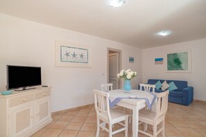 Ein Essbereich mit Tisch, Stühlen, einem Fernseher auf einem Schrank und einem blauen Sofa im Hintergrund.