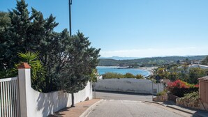 Une rue résidentielle avec vue sur la mer, une clôture blanche et quelques espaces verts.