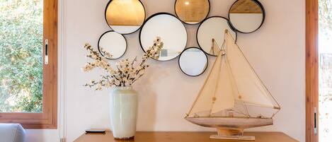 A wooden dresser with a vase of flowers, a scale model sailboat, and multiple round mirrors on the wall.