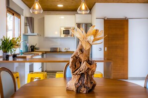 Une table à manger agrémentée d’un centre de table composé d’une souche d’arbre et d’épis de maïs, une chaise jaune et un plafond en bois.