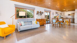 A modern living room with a sofa, a dining table with chairs, a kitchen area with a refrigerator, and a wooden ceiling. - Vacation Home Santa Eulàlia 54 with Wi-Fi, A/C, Pool, Garden & Terrace; Parking Available (Can Picafort)