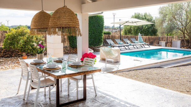 An outdoor patio with a pool, white chairs, a dining table, and hanging lamps. - Vacation Home Santa Eulàlia 54 with Wi-Fi, A/C, Pool, Garden & Terrace; Parking Available (Can Picafort)