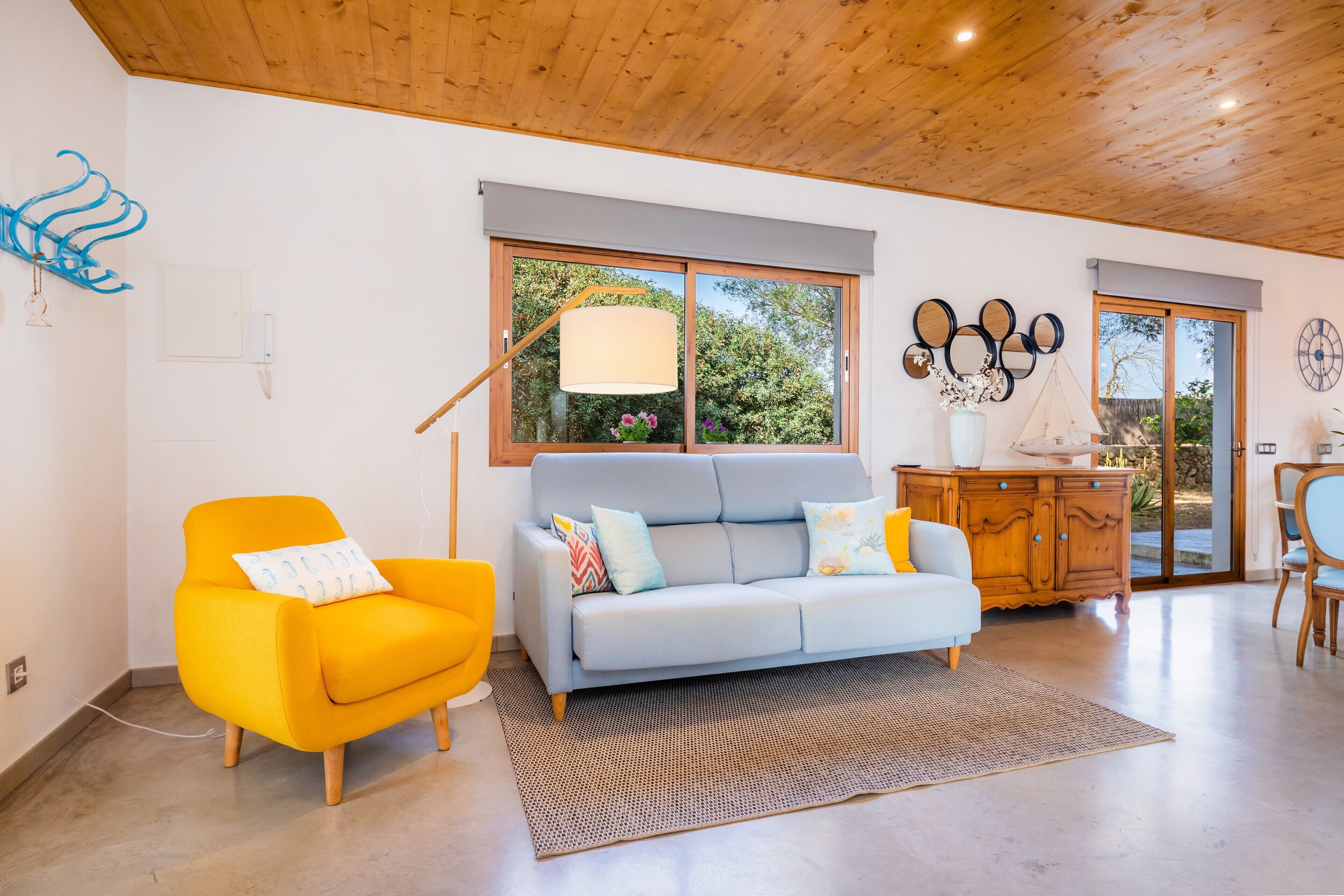 Un salon moderne avec un canapé, un fauteuil jaune vif, un meuble en bois et une grande fenêtre.