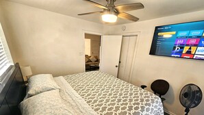 A bedroom with a bed, a ceiling fan, a TV mounted on the wall displaying a Roku interface, and a door leading to another room. - Bonita-Jamaica Beach w/Pool,Dog Friendly,kayak/pdlebrd,big yard,8min walk 2beach (Jamaica Beach)