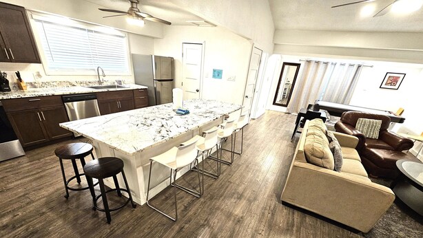 A modern kitchen with a central island, bar stools, and a dining area with a sofa and chairs. - Bonita-Jamaica Beach w/Pool,Dog Friendly,kayak/pdlebrd,big yard,8min walk 2beach (Jamaica Beach)