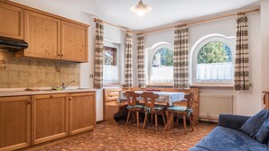 A kitchen with wooden cabinets, a dining table with chairs, and a blue sofa. - Holiday Apartment Casa Lorenz 2 with Mountain View, Wi-Fi & Garden (Canazei)