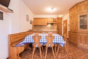 A kitchen with wooden cabinets, a tiled backsplash, a table with a checkered tablecloth, and wooden chairs.