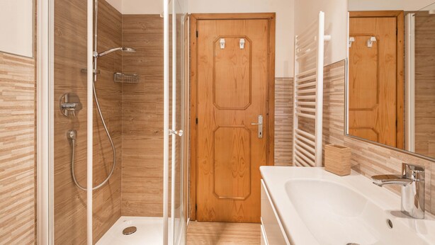 A bathroom with a shower, a sink, a mirror, and a wooden door.