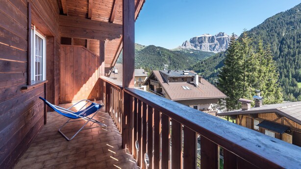 Ein Holzbalkon mit blauem Stuhl, Holzgeländern und Blick auf die Berge.