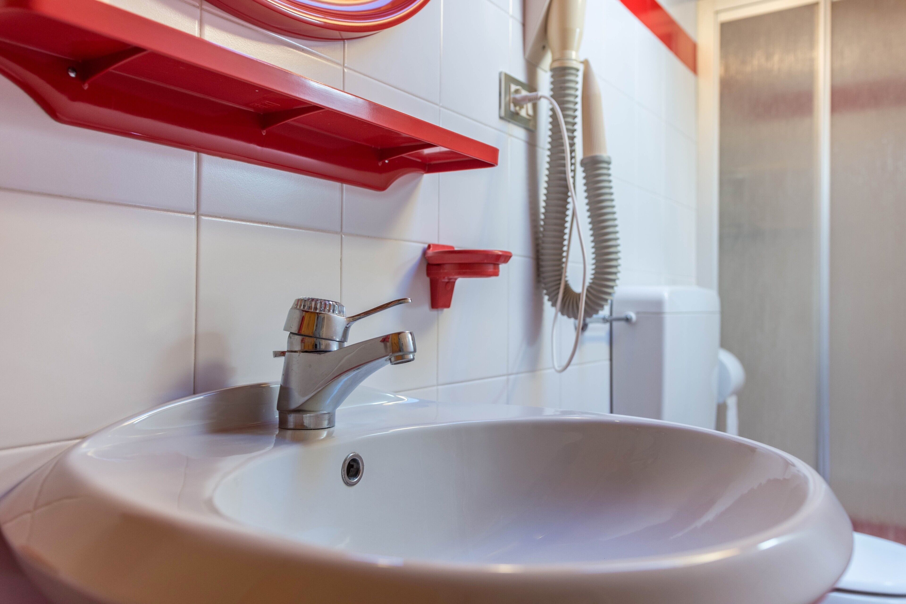 A bathroom with a white sink, red towel rack, and a hairdryer on the wall.