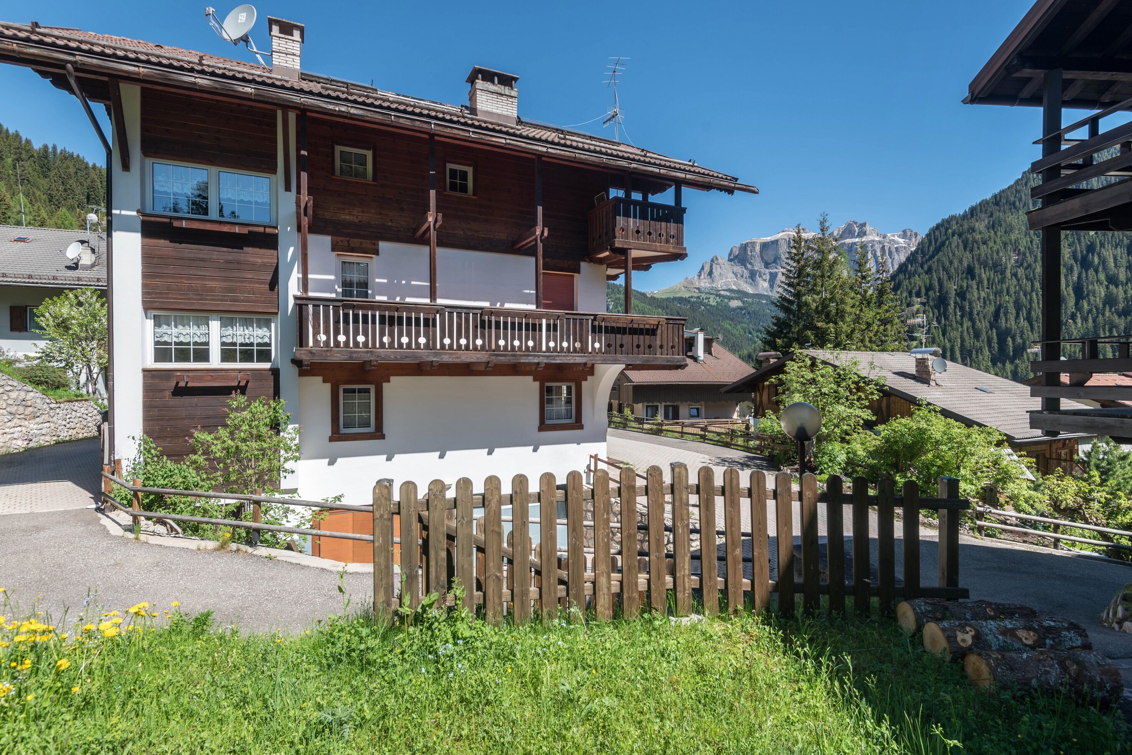 A two-story wooden chalet with balconies, a wooden fence, and a mountainous backdrop.