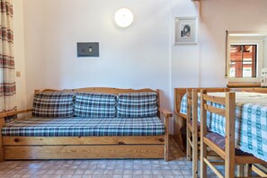 Un canapé en bois avec des coussins à carreaux, une lampe fixée au mur, un tableau encadré et une fenêtre donnant sur un paysage.