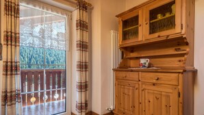A room with a wooden cabinet, a radiator, and a view of a balcony with patterned curtains.