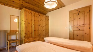 A bedroom with two beds, wooden wardrobe, and a chair.
