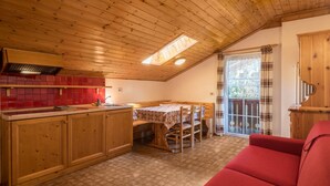 A kitchen with wooden cabinets, a red tiled backsplash, a dining table with chairs, and a red sofa.