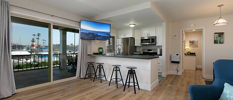 A modern kitchen with a bar area, a large TV, and a view of the marina.