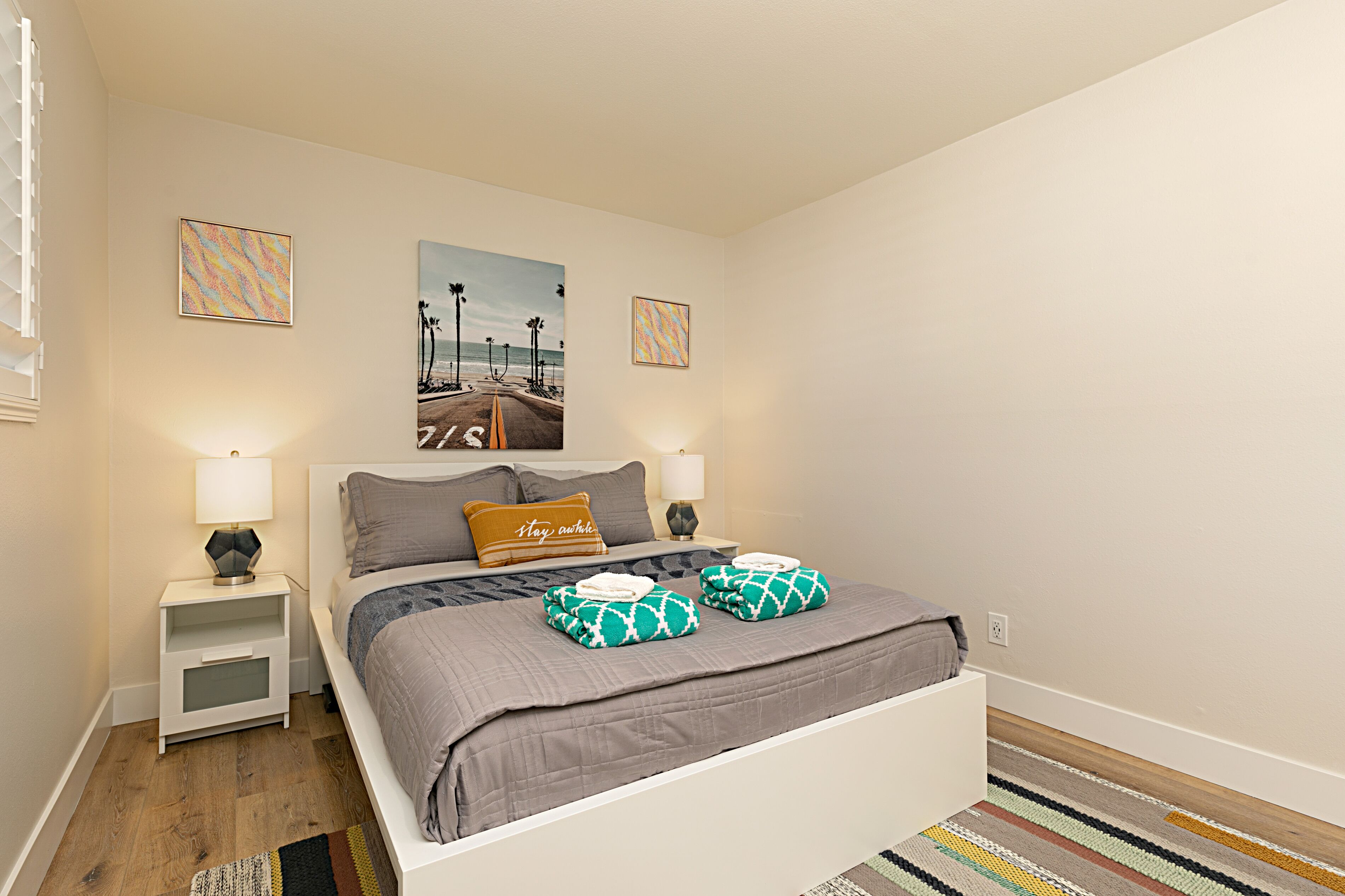A neatly arranged bedroom with a bed, two nightstands, a rug, and two wall art pieces.