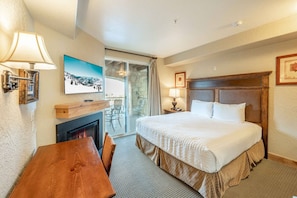 A hotel room with a bed, a fireplace, a dining table, and a view of the outdoors. - Silverado Lodge at Canyons Village  | 122ABC (Park City)