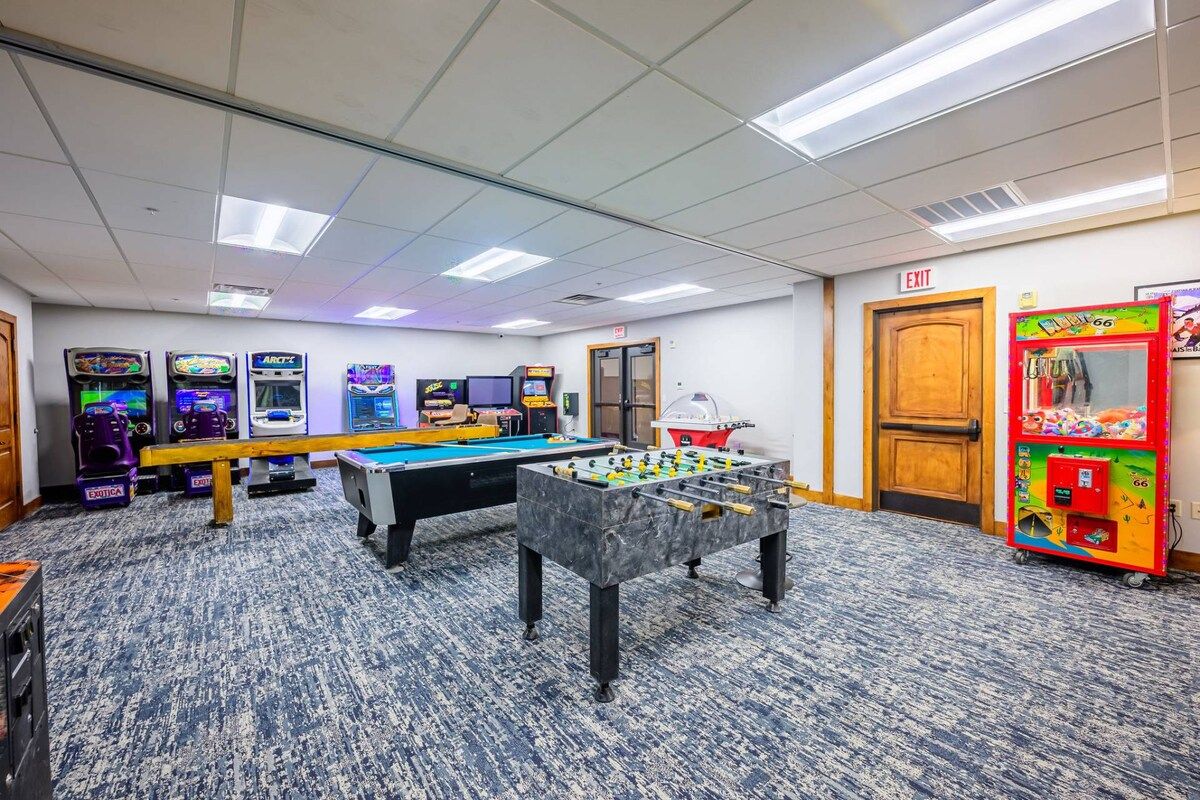 A room with a foosball table, multiple arcade machines, and a pool table.