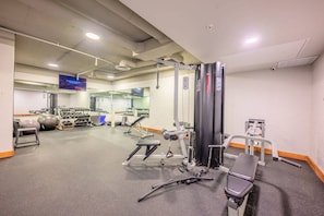 Un gimnasio con varios equipos de ejercicio, incluyendo mancuernas, una banca y una estructura para sentadillas.