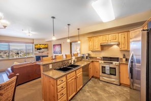 A kitchen with granite countertops, wooden cabinets, stainless steel appliances, and a large window offering a view. - Silverado Lodge at Canyons Village  | 122ABC (Park City)